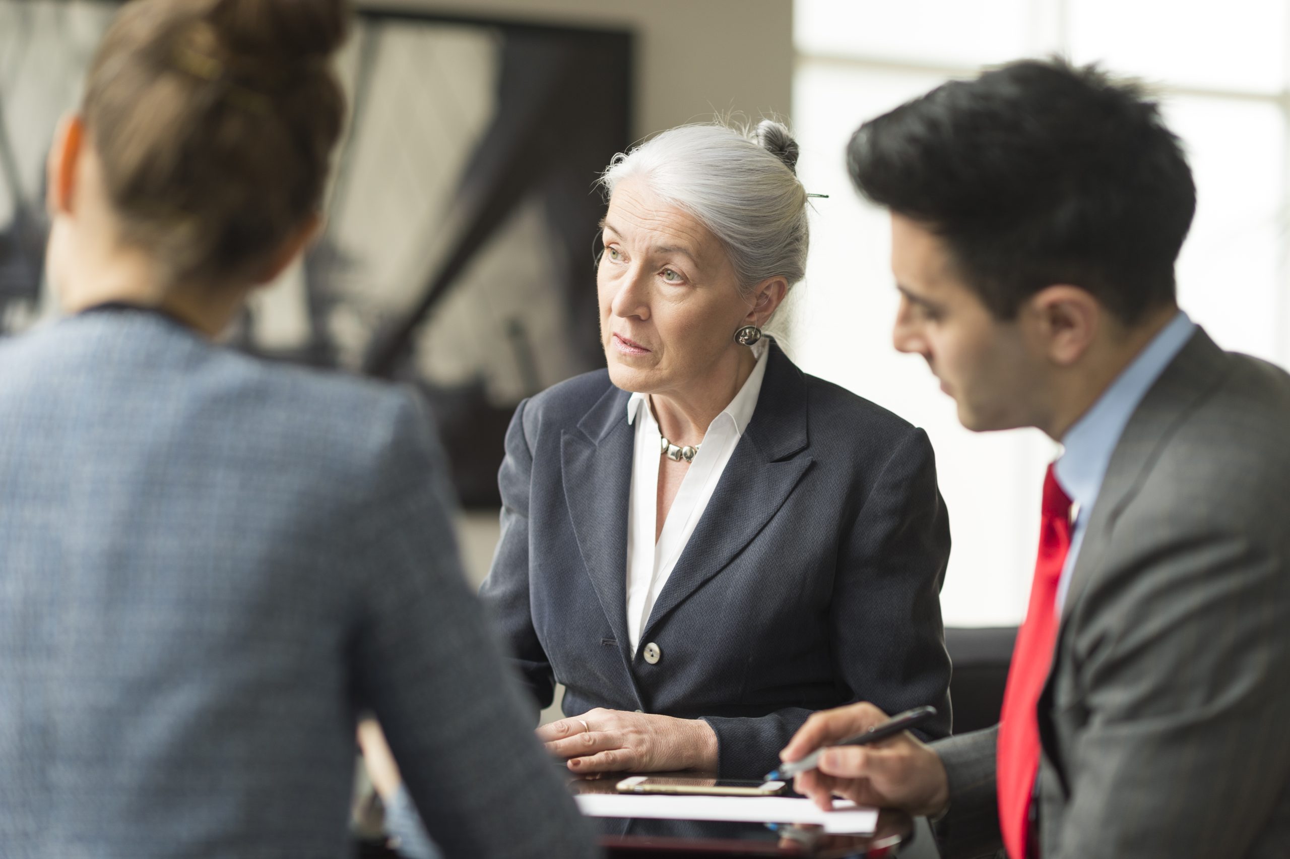 Three business professionals engaged in a discussion in a modern office setting.