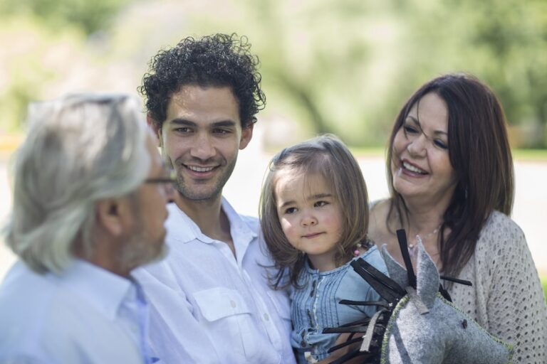 Multigenerational family outdoors, smiling adults and young girl holding gray stuffed horse toy.