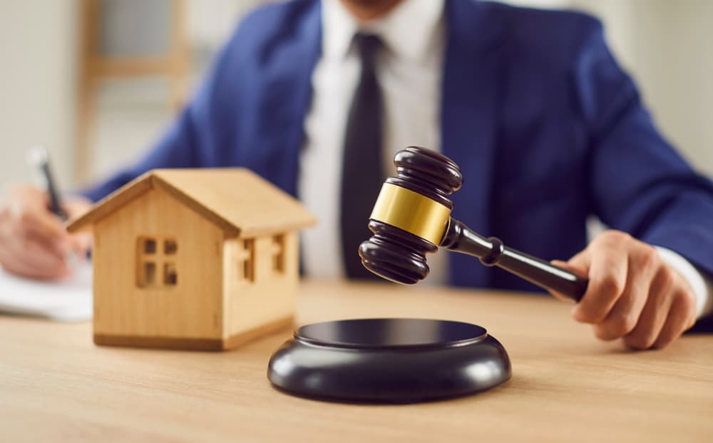 Probate Lawyer sitting at desk with gavel and small wooden toy house, working with documents.
