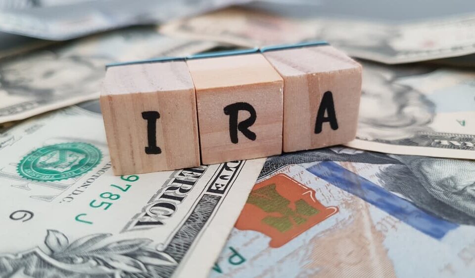 IRA acronym made of wooden letter cubes on pile of US dollar banknotes.