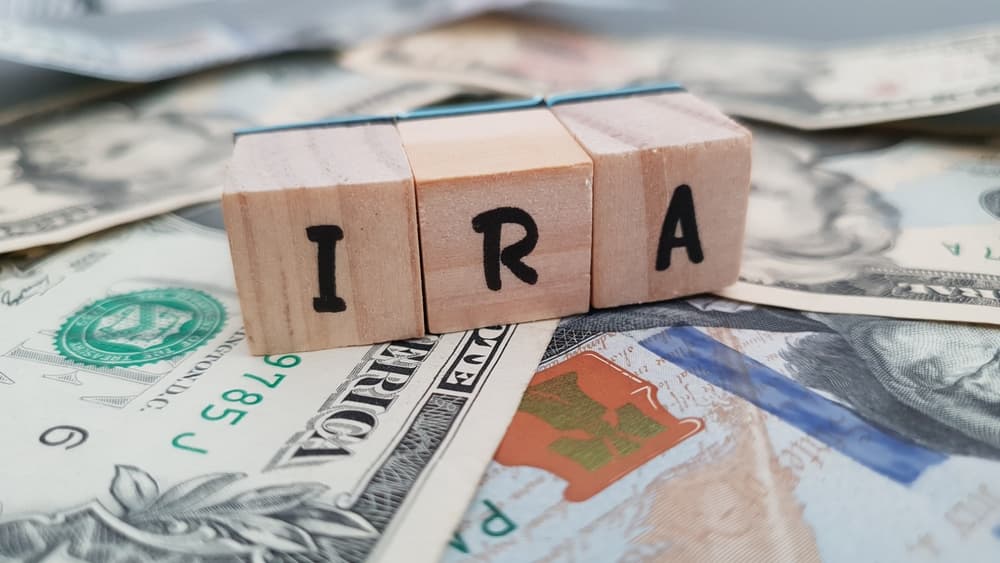IRA acronym made of wooden letter cubes on pile of US dollar banknotes.