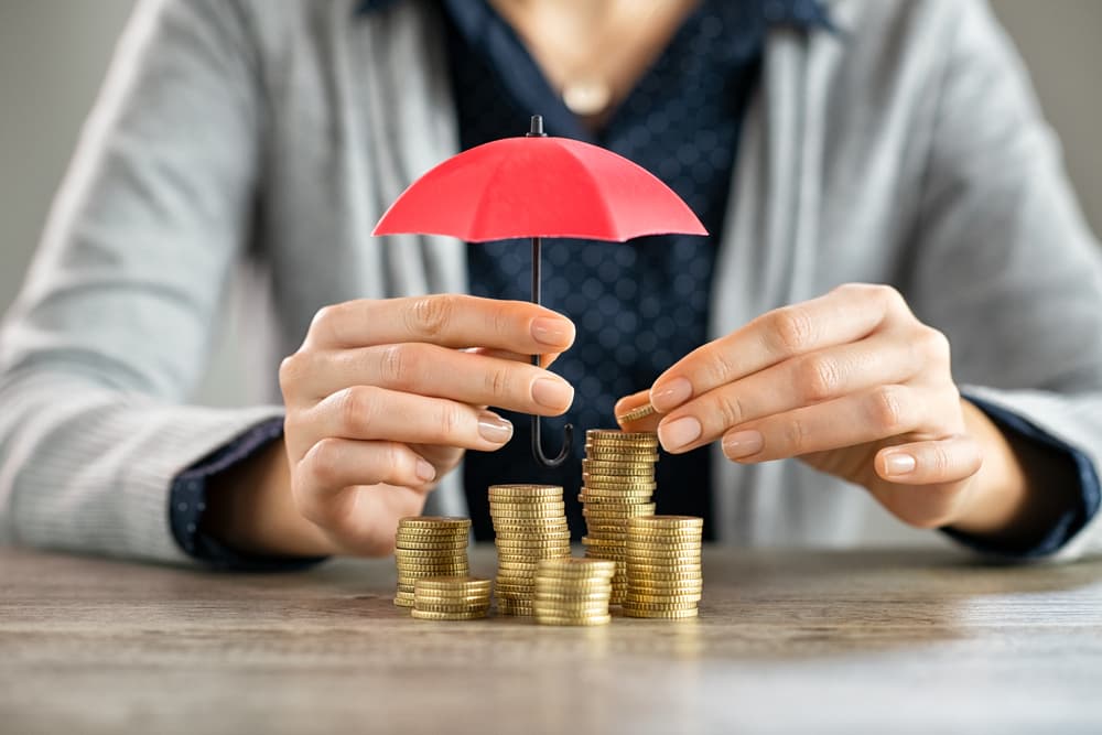 Young woman hands holding red umbrella over stacked coin on table.