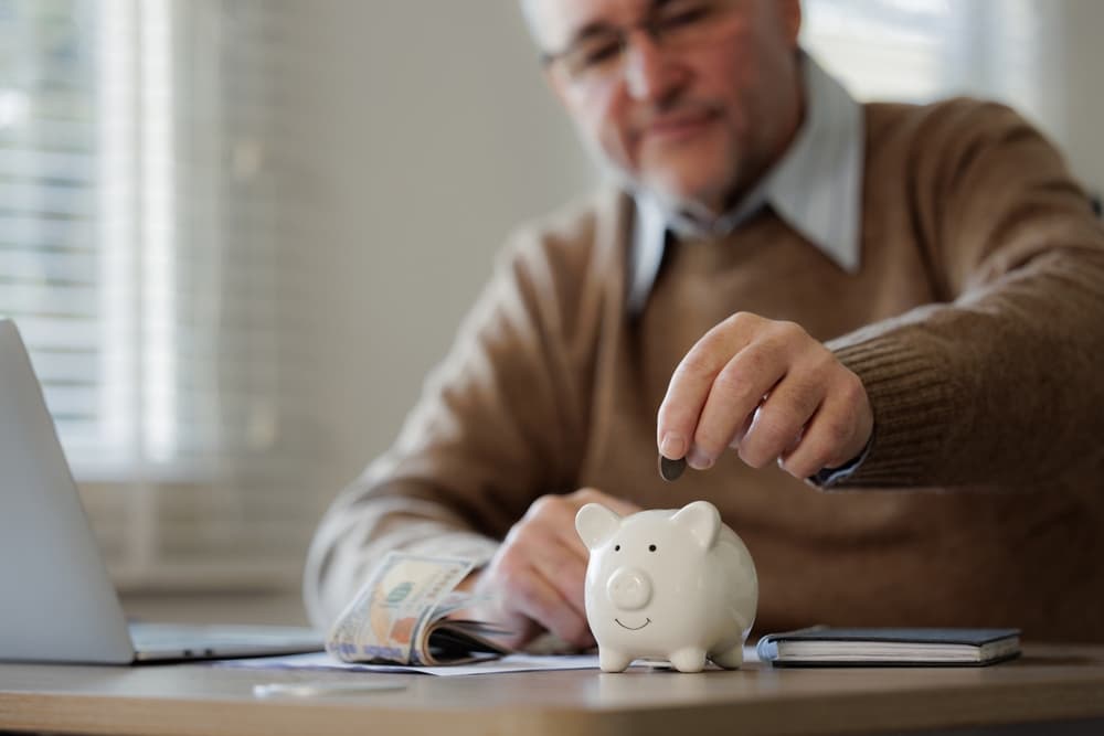 Senior man putting money coin in piggy bank