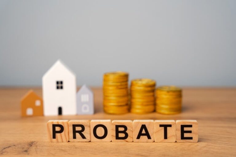 Wooden letter blocks spelling "PROBATE" in front of miniature house models and stacked gold coins.
