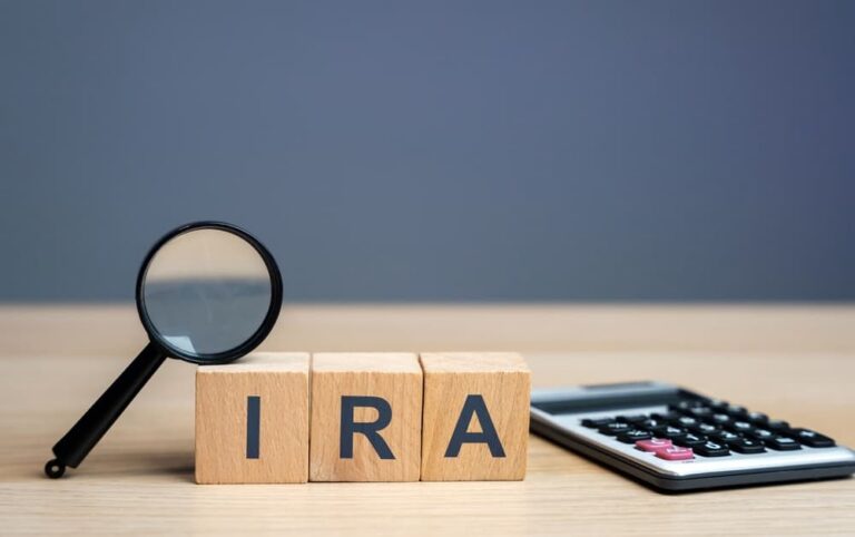 Wooden blocks spelling "IRA" with a magnifying glass and calculator on a wooden surface.