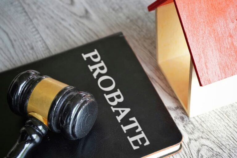 Black gavel resting on a probate book beside a small wooden house model with a red roof.