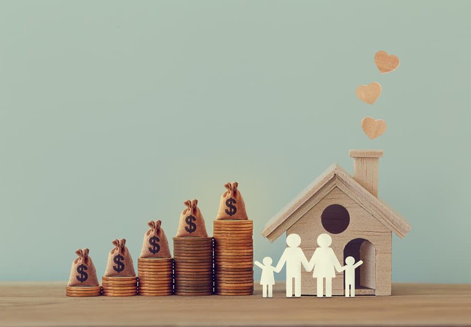 Mini house and heart, family members, US money bags on rows of rising coins on table.