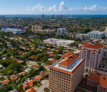 Aerial view of a coastal cityscape with residential and commercial buildings under a partly cloudy blue sky.