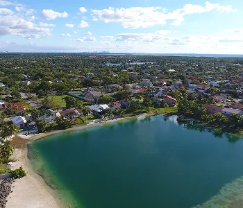 Aerial view of a residential neighborhood surrounding a calm blue lake under a partly cloudy sky.