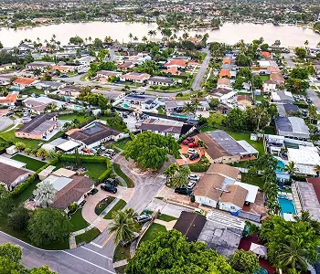 Aerial view of a suburban neighborhood with houses, trees, and a river in the background.