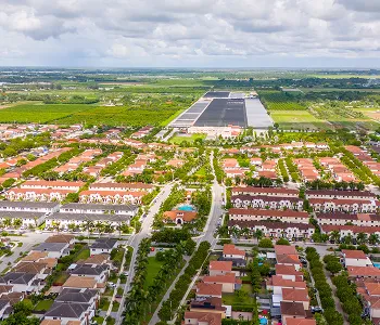 Aerial view of a suburban neighborhood with rows of houses and green spaces under a cloudy sky.