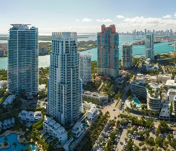 Aerial view of modern high-rise buildings along a waterfront with a city skyline in the distance.