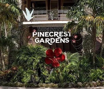 Entrance sign for Pinecrest Gardens surrounded by lush greenery and red floral decorations.