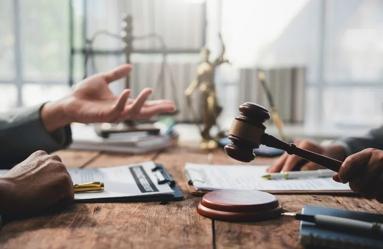 Two people discussing legal documents at a wooden table with a judge's gavel and scales of justice in the background.