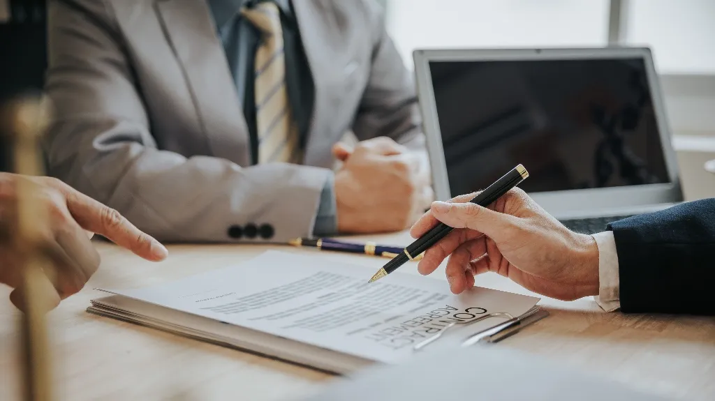 Two business professionals reviewing a contract agreement with a laptop on a wooden table.