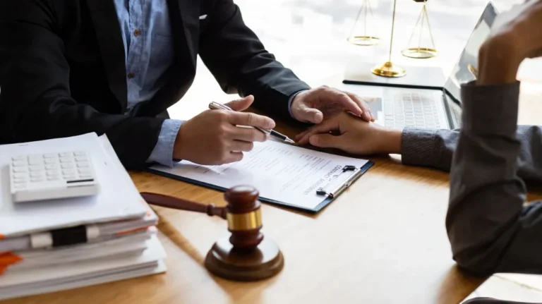Two professionals discussing a contract agreement at a wooden desk with legal symbols.