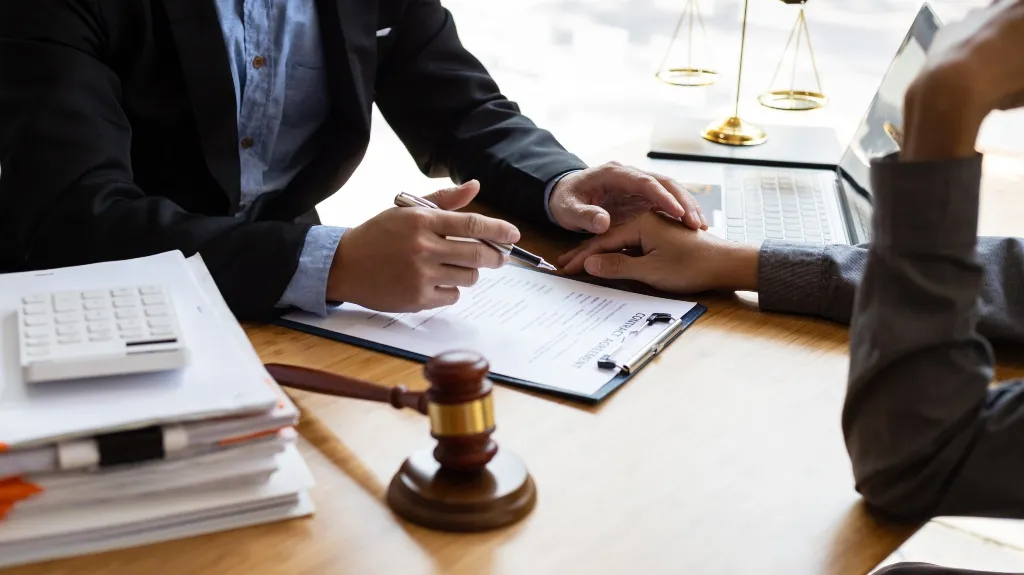Two professionals discussing a contract agreement at a wooden desk with legal symbols.