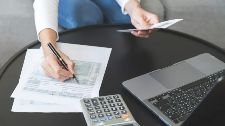 Person reviewing and signing documents at a black table with laptop and calculator.
