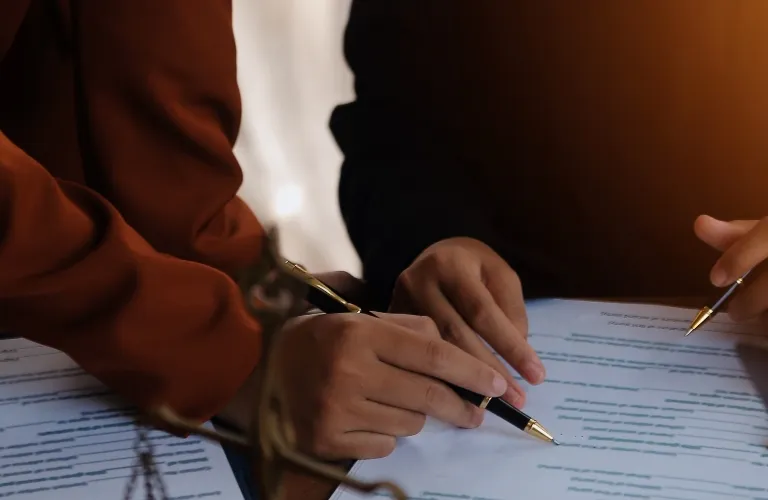 Two individuals in brown and black sleeves reviewing and annotating documents with pens.