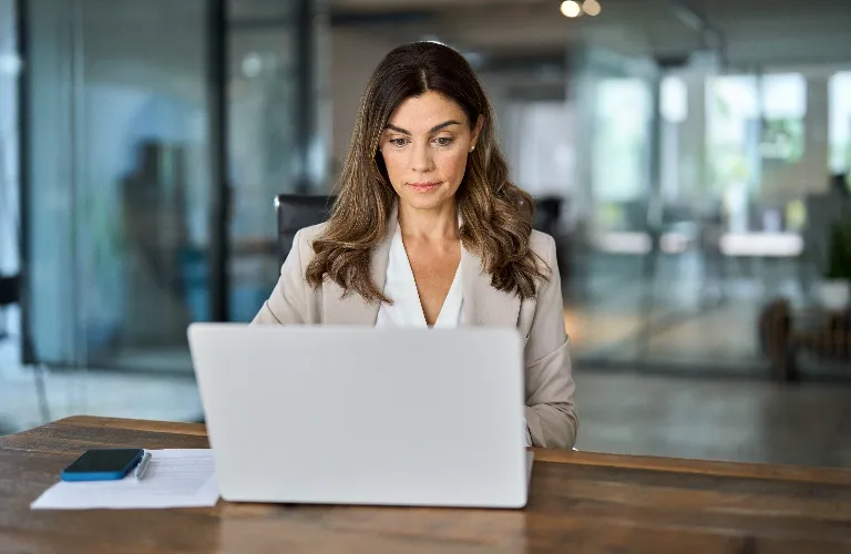 Professional woman with brown hair working on a laptop in a modern office setting.
