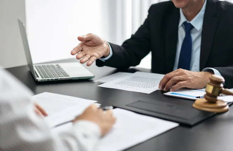 Two professionals in suits discussing documents at a desk with a laptop and gavel.