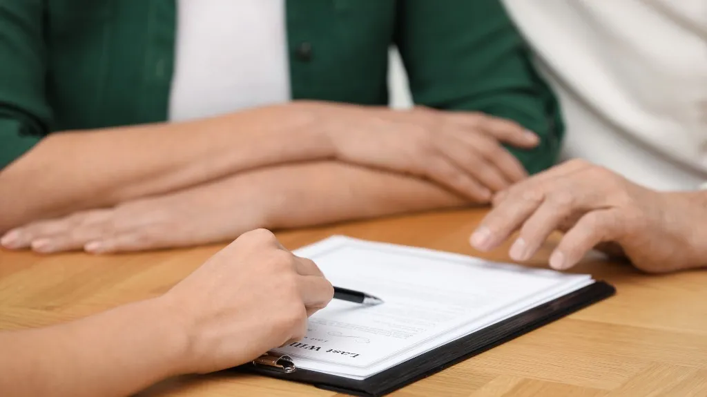 Close-up of three people with folded arms and hand pointing at a document on a wooden table.