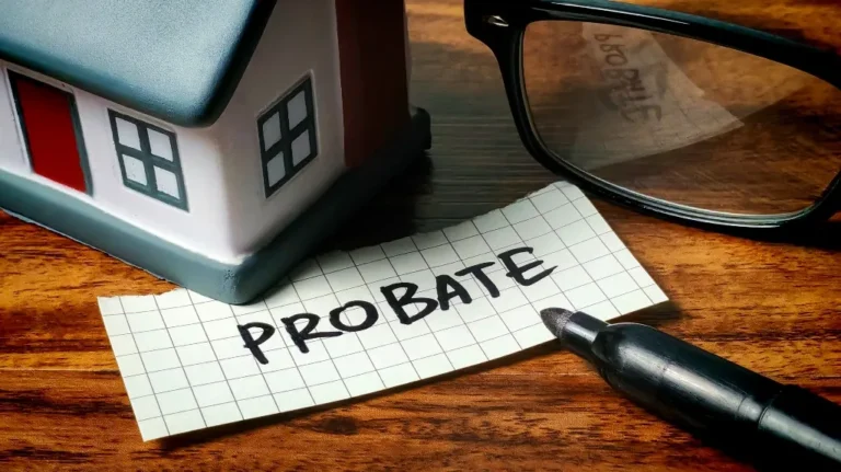 Small model house, black marker, eyeglasses, and paper with "PROBATE" written on wooden surface.
