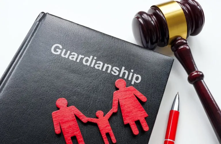 Black book titled "Guardianship" with red family figures, wooden gavel, and red pen on white surface.