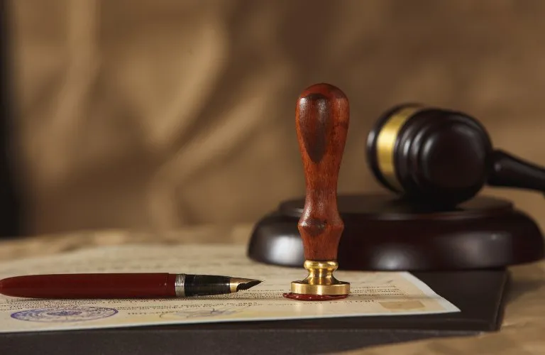 Wooden stamp, fountain pen, and judge's gavel on legal document with beige background.