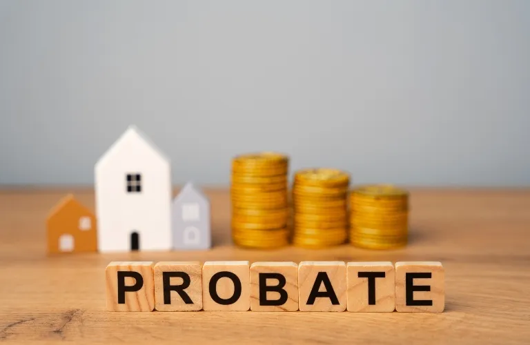 Wooden blocks spelling "PROBATE" in front of miniature house models and stacked gold coins.