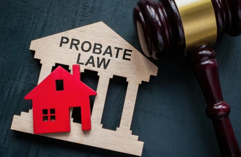 Wooden house model and "Probate Law" sign next to a judge's gavel on dark surface.